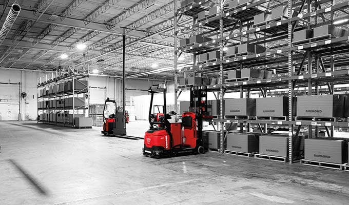 Black and white view of inside of a warehouse of a Red Raymond forklift moving pallets.
