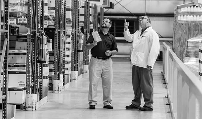 Black and white view of inside of a warehouse of two people talking 
