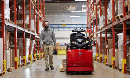 Image of Raymond Forklift equipped with Advance Operator Assist Technology  with operator walking parallel to the truck in a warehouse. 