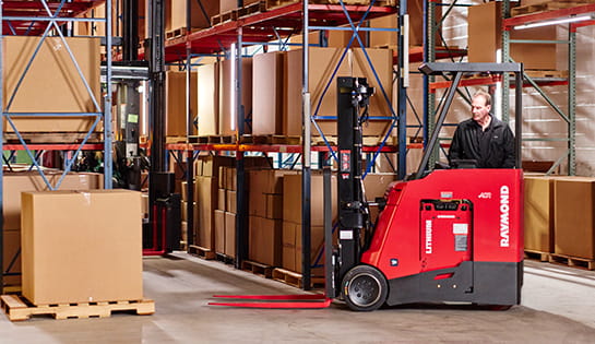 Raymond stand-up forklift navigating warehouse aisle with palletized inventory