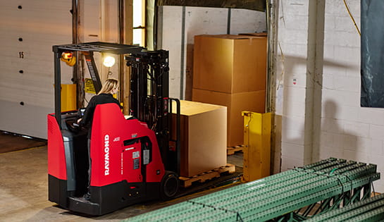 Raymond stand-up forklift unloading pallet at warehouse loading dock.