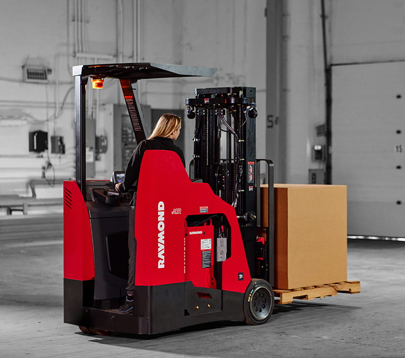 Raymond 4260 stand-up counterbalanced forklift transporting pallet in warehouse